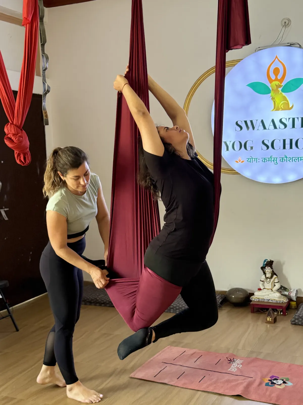 Aerial yoga teacher assisting a student in the hammock