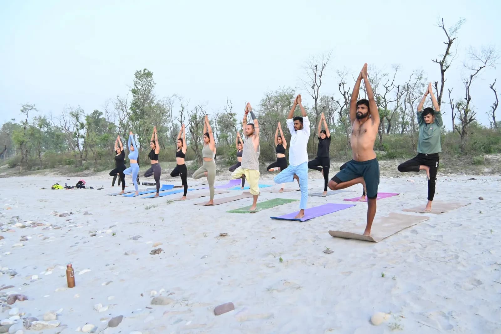 Yoga teacher training students holding Tree pose together on the Ganga beach in Rishikesh