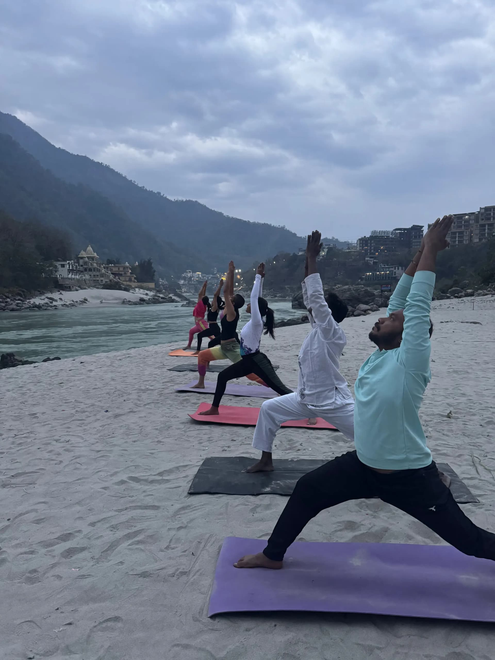 100 hour yoga teacher training students in Warrior II on the Ganga beach in Rishikesh