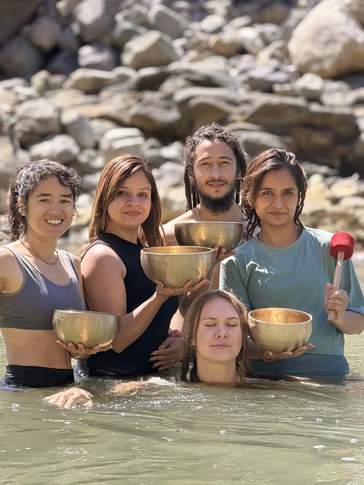 Sound healing students playing Tibetan singing bowls while sitting in the Ganga